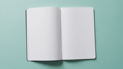 Close-up-of-open-blank-book-with-copy-space-on-green-background-in-slow-motion