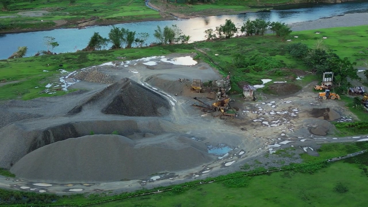 Orbiting aerial view of rock quarry and crushing site along tropical island river in the Philippines.
