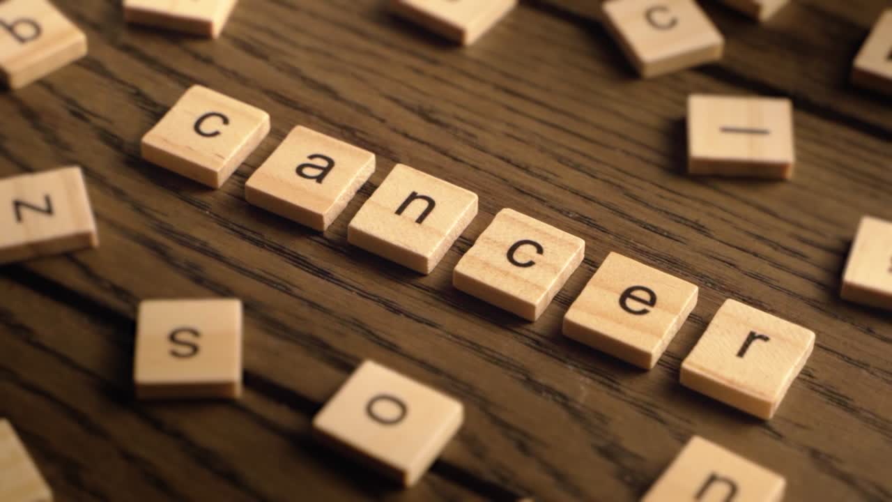 Wooden tiles spell the word cancer as the camera pans across a rustic wood surface with warm, cinematic lighting.