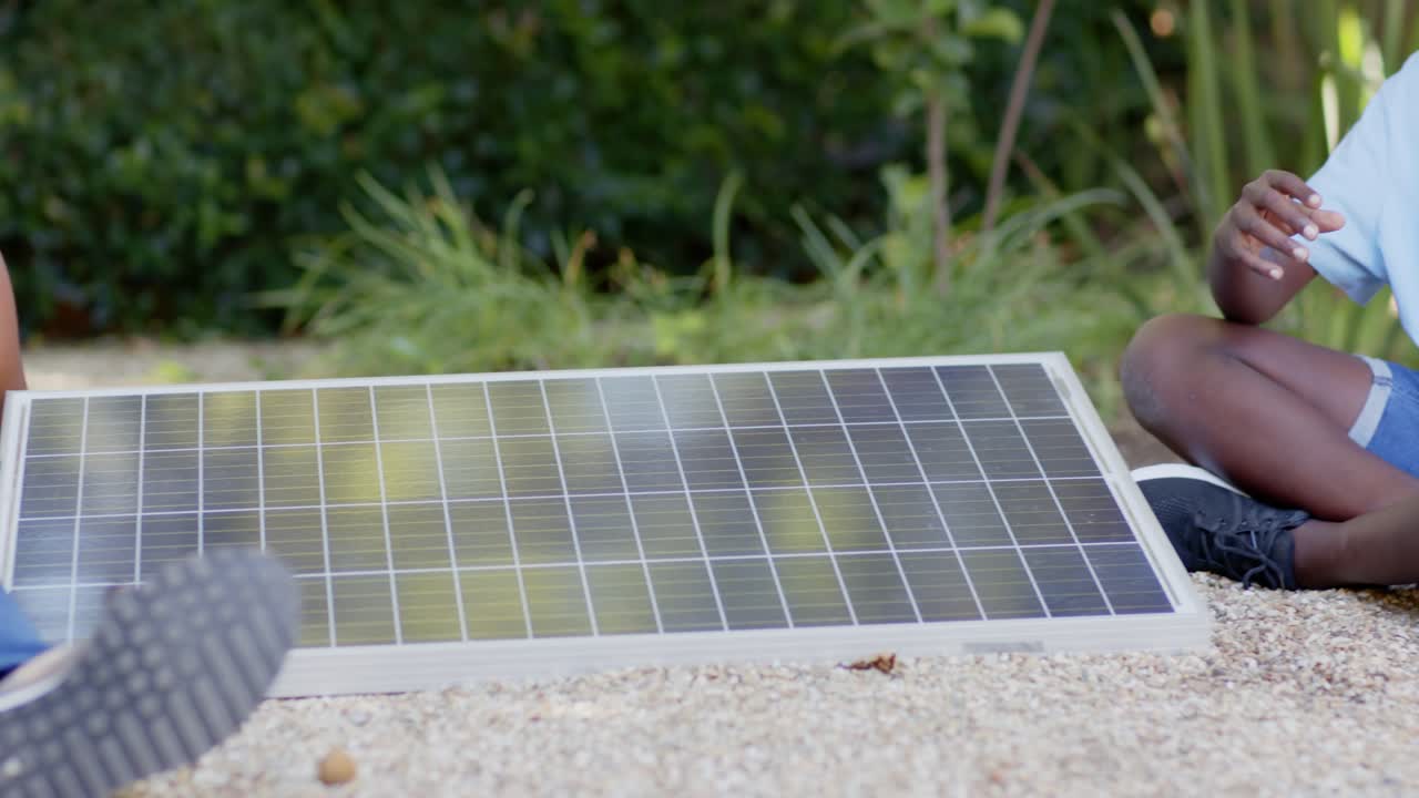 Padre e figlio adolescente presso un pannello solare in giardino, il figlio indica il sole mentre il padre posiziona il tablet, controllando l'angolazione.