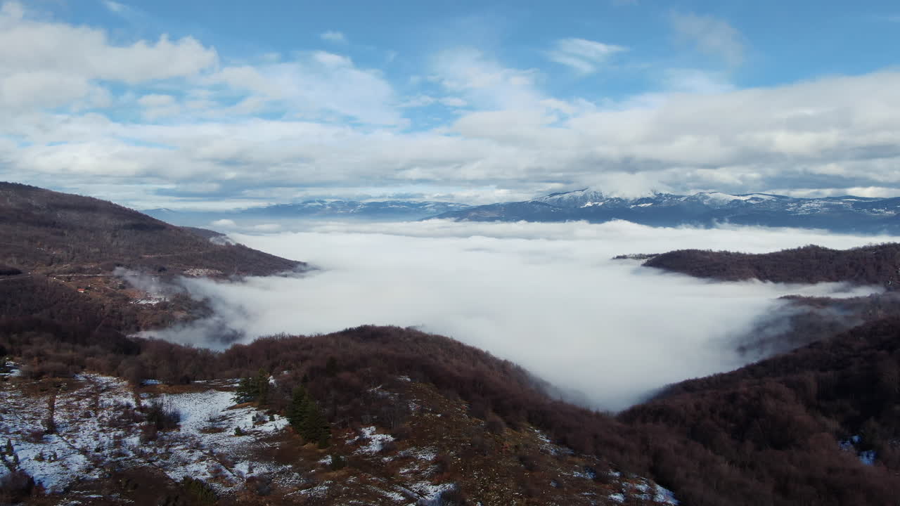 A view of hills partially covered in fog with mountains visible in the distance under a cloudy sky Landscape with fog and hills