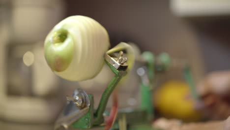 A woman's hands operating a manual apple peeler in the kitchen
