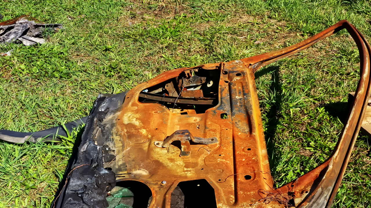 Closeup of rusted car door burnt by fire lying on grass in abandoned outdoor setting
