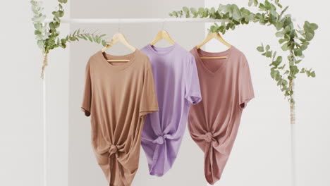 video de primer plano de camisetas blancas, beige y púrpuras colgando sobre un fondo blanco