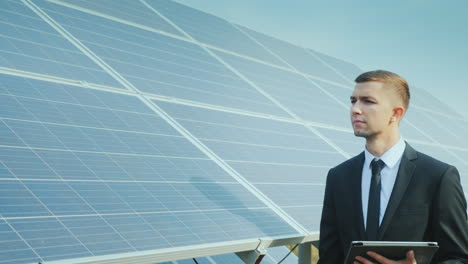 Businessman-With-A-Tablet-In-His-Hands-Goes-Along-A-Row-Of-Solar-Panels-Development-Of-Alternative-E