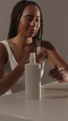 studio skincare beauty shot of woman dispensing moisturiser from bottle into hand 1