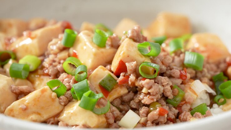 Making stir-fried mapo tofu with hot spicy sauce and scallion over white rice in a bowl at home