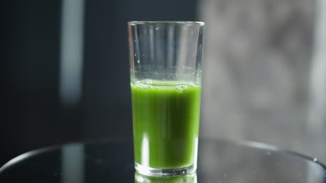 half-full glass of green juice with natural backlight and bubble details