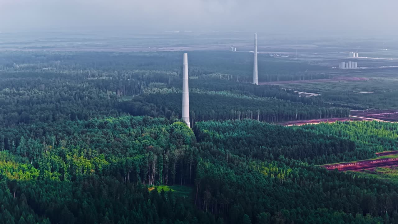 Circling drone shot of tall white wind turbine towers without nacelles being built within a vast green pine forest in rural Latvia