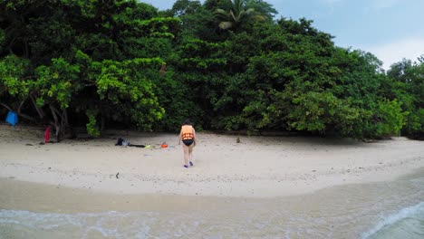Women-in-life-vest-and-a-hat-walks-out-of-the-the-water-into-tropical-island