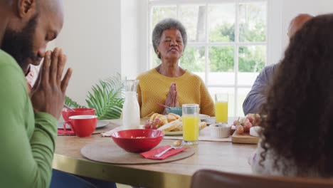 Video-of-happy-african-american-parents,-daughter-and-grandparents-saying-grace-at-dinner-table