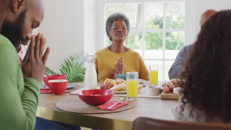 video de padres afroamericanos felices, hija y abuelos diciendo la gracia en la mesa de la cena