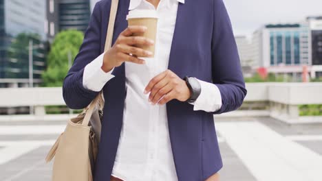 african american businesswoman holding takeaway coffee and checking smartwatch