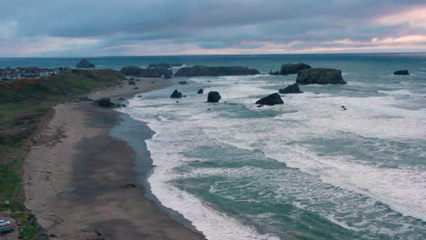 Aerial-of-Bandon-beach-and-houses-on-the-bluff-during-evening-hours,-with-steady-waves-coming-ashore