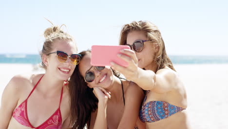 Three-teenage-girl-friends-taking-selfie-on-beach-wearing-colorful-bikini-sharing-vacation-photo