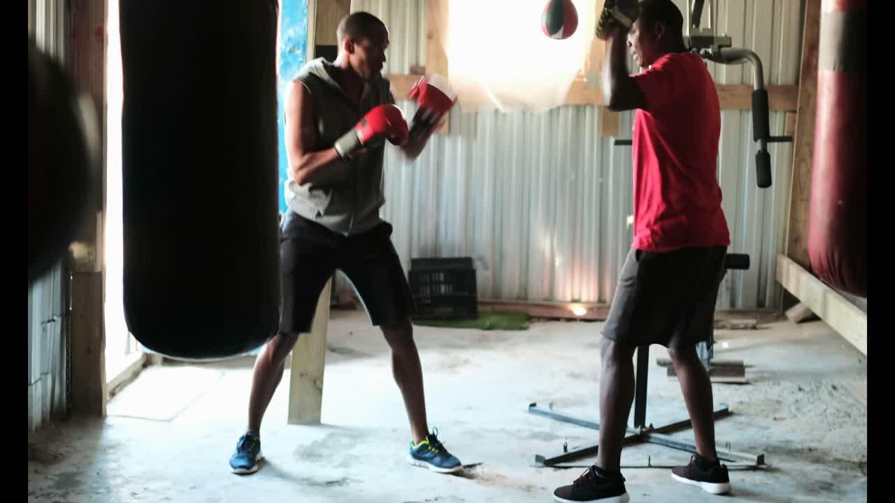 African American male boxer practicing boxing with trainer in fitness studio 4k
