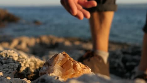 Mann-Findet-Glänzendes-Calcit-Mineralgestein-An-Felsen-Am-Meer