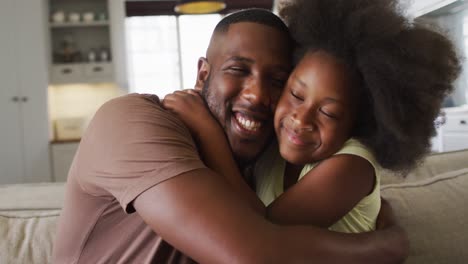 african american daughter and her father smiling and embracing on couch