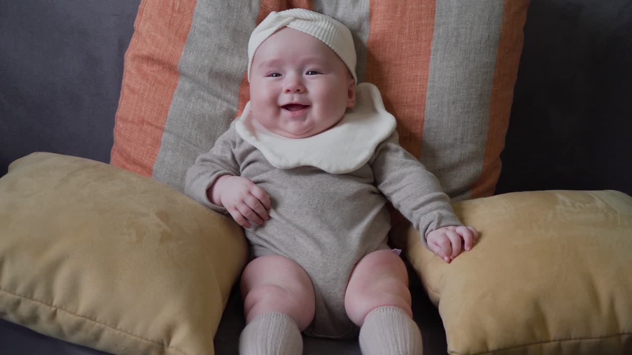 턱받이와 헤드밴드를 착용한 쿠션을 들고 소파에 혼자 앉아 있는 사랑스러운 어린 소녀