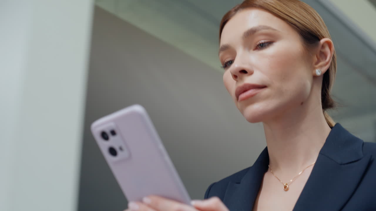 Elegante donna che guarda il cellulare mentre cammina nel corridoio di un ufficio moderno, primo piano