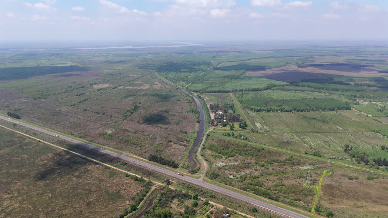 RN12 national roadway bends through vast open wetlands and cultivated fields near the Paraná Delta in Argentina, revealing sparse vegetation and hydrological features, aerial view