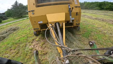 vista del punto de enganche entre el tractor y la empacadora de heno redonda mientras remolca la empacadora a lo largo de la hilera de alfalfa