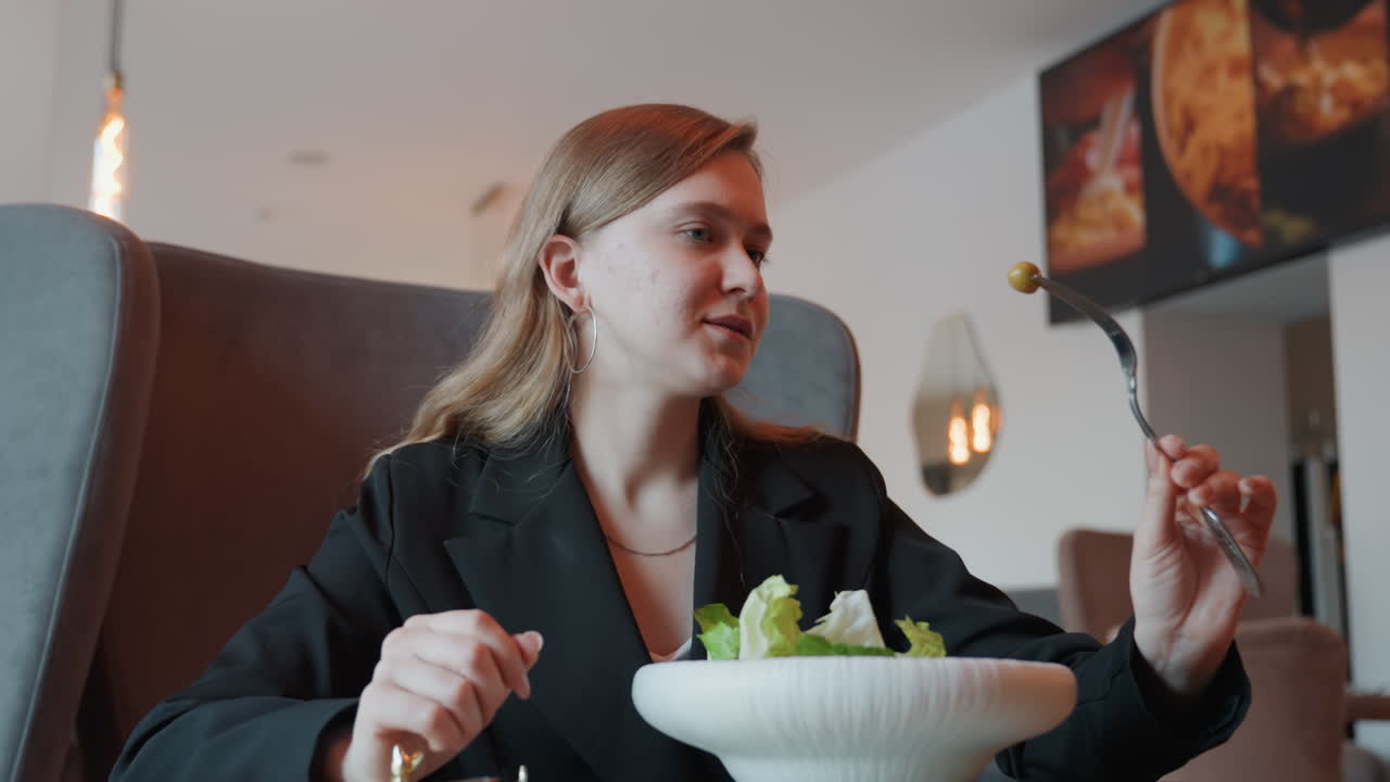 Weiße Frau genießt Business-Lunch-Salat in modernem Restaurant, Blazer und selbstbewusstes Lächeln, Gabel mit Grünzeug über der Schüssel, professionelle Lifestyle-Darstellung, frischer Salat und Dressing, stimmungsvolles Ambiente.