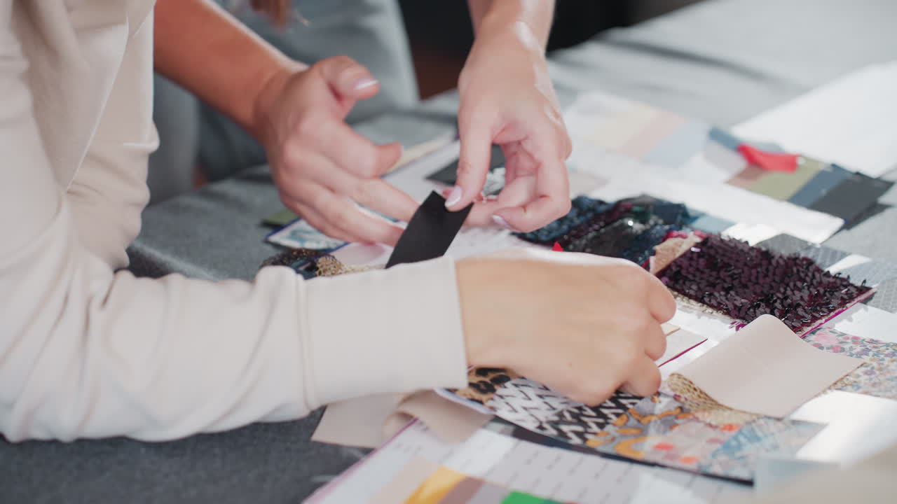 Costumer carefully comparing black textile sample against fair skin tone during creative design selection session, analyzing color compatibility and texture among various fabric swatches