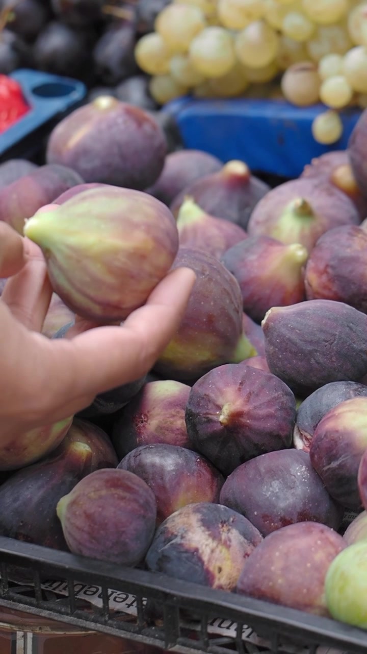 A Hand Picks a Fresh Fig from a Crate at a Market