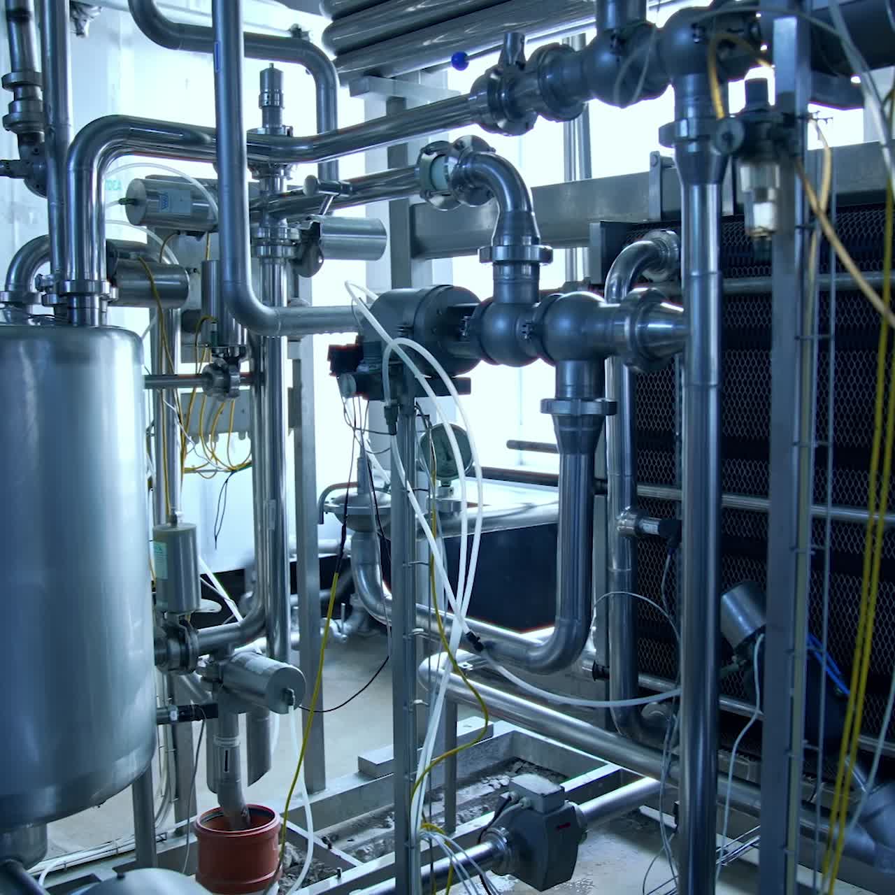 Stainless pipes and tubes as part of the equipment at modern dairy production. Metal tubes and big tank at the backdrop of large window. Silver pipes joined and crossed with each other