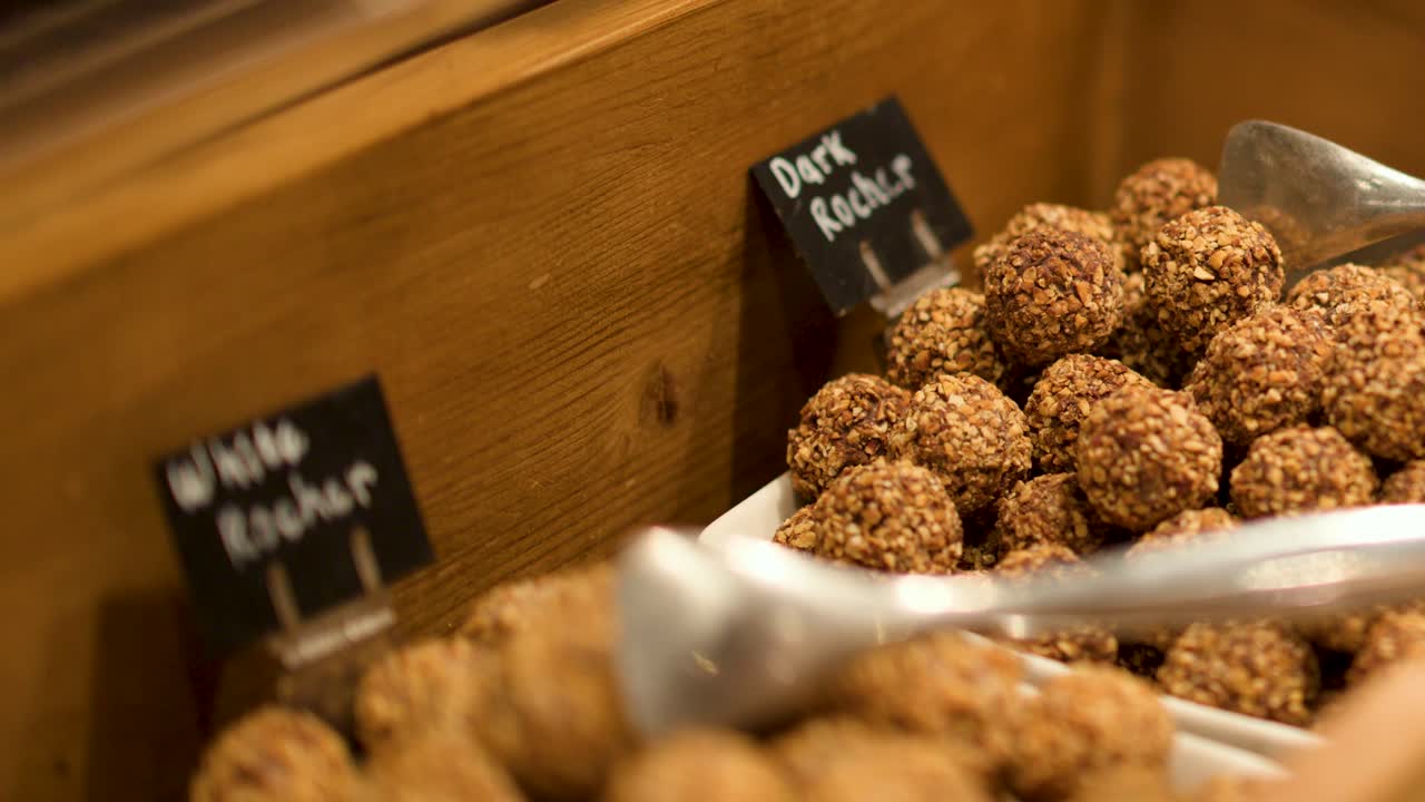 Warmly lit chocolate truffles in display case, shallow focus, gentle camera movement, evening ambiance