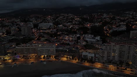 illuminated cityscape of torreblanca, spain, revealing an aerial view at dusk, where urban sprawl meets the tranquil sea under a darkening sky, drone ascending shot