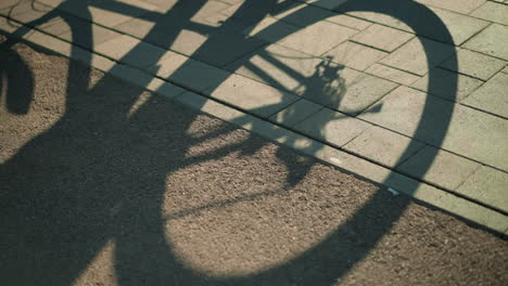 shadow of upside-down bike cast on ground, with back tire rotating and someone standing close, capturing a dynamic silhouette effect under warm sunlight on pavement