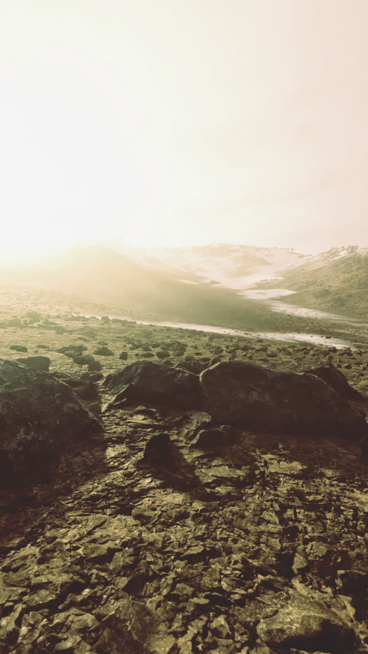 Vast rocky landscape illuminated by warm sunlight near distant mountains
