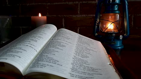 pick up open bible on table with candle and oil lamp