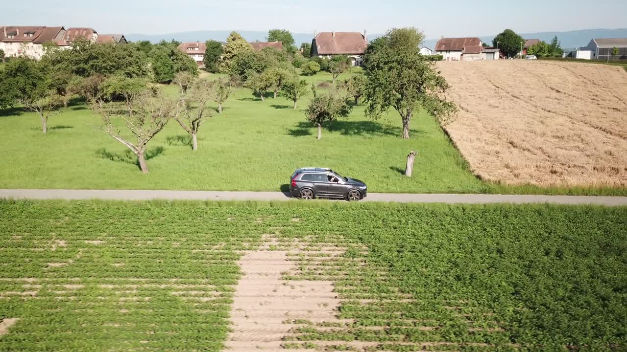 un camión suv volvo xc 90 se mueve a un ritmo lento en una carretera entre campos destinados a la agricultura, campo, suiza, vaud, toma aérea de drones