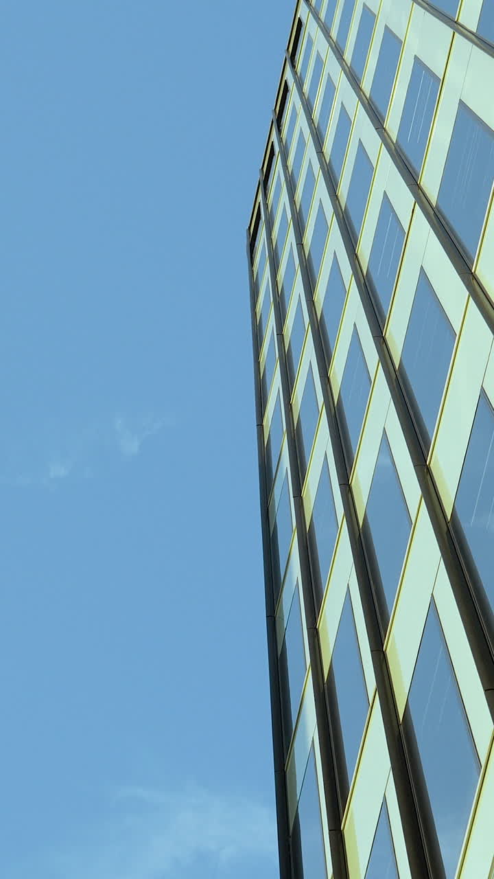 Una perspectiva vertical en contrapicado de un edificio de oficinas contemporáneo con ventanas de cristal que reflejan el cielo azul. Ideal para contenido corporativo, desarrollo urbano e inmobiliario