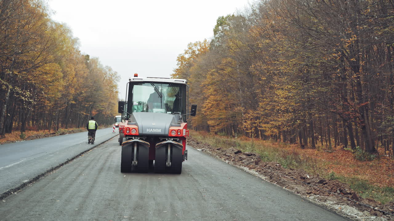 Asphalt roller that stuck and press hot asphalt while making a new road in autumn. Road repair machines with heavy vibration rollers compactor are working on a road.