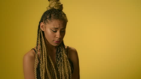 Confused-woman-with-afro-hairstyle-twirling-hand-on-yellow-background-in-studio