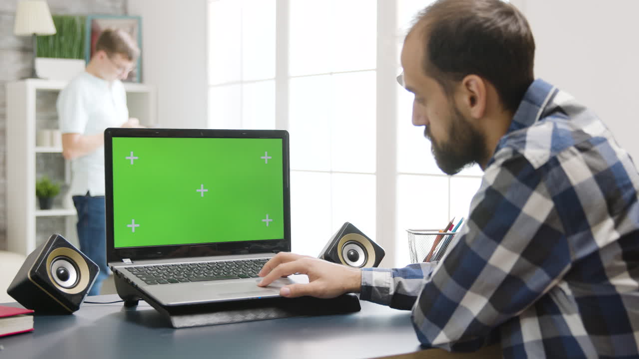 Man working on laptop with green screen at home