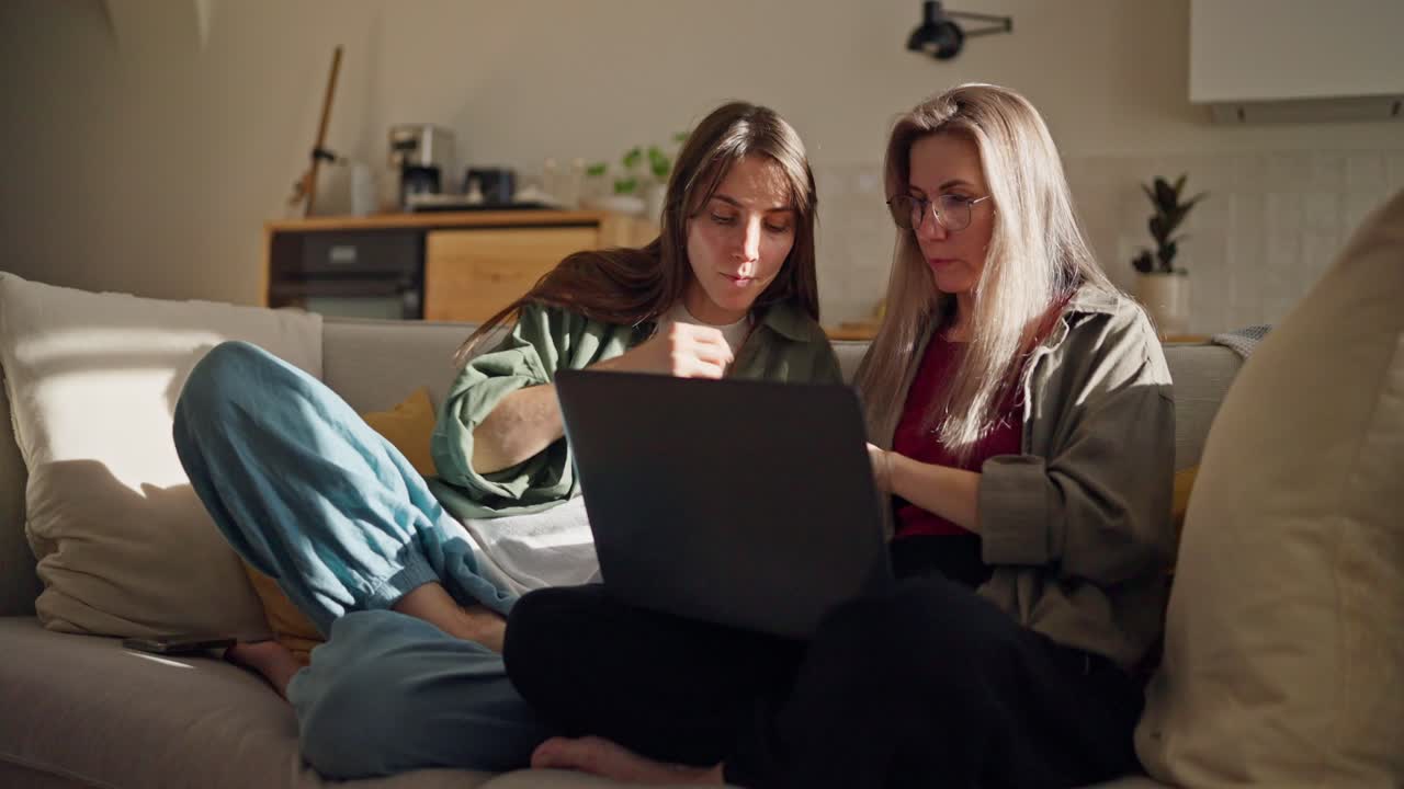 dos mujeres mirando una computadora portátil en un sofá