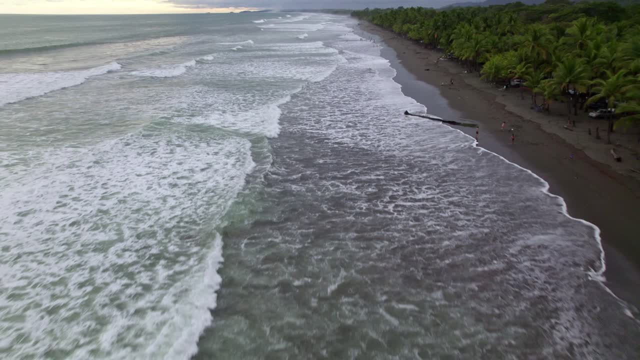 Dolly aereo che sorvola onde marine turchesi e spumeggianti che si infrangono sulla costa vicino a una fitta giungla a Dominicalito Beach, Costa Rica.