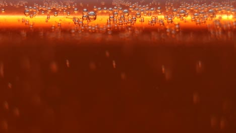 abstract veiw macro close-up of a glass of beer beverage with active fizzy bubbles of co2 gas, carbon dioxide orange gold background