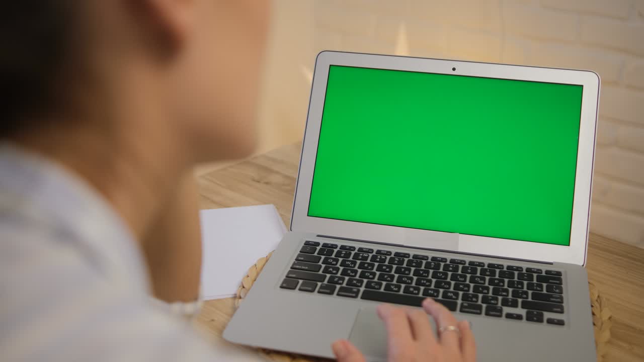 Green computer screen. The girl sits at the table and remotely learns, works. Surfs the Internet. A girl in a striped pajama top. Rear view. Close-up
