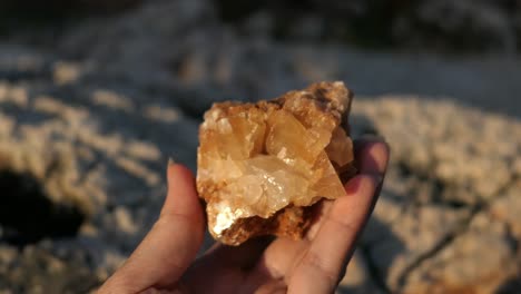 Woman-holding-shiny-calcite-mineral-rock-crystal-in-rocky-shore,-point-of-view