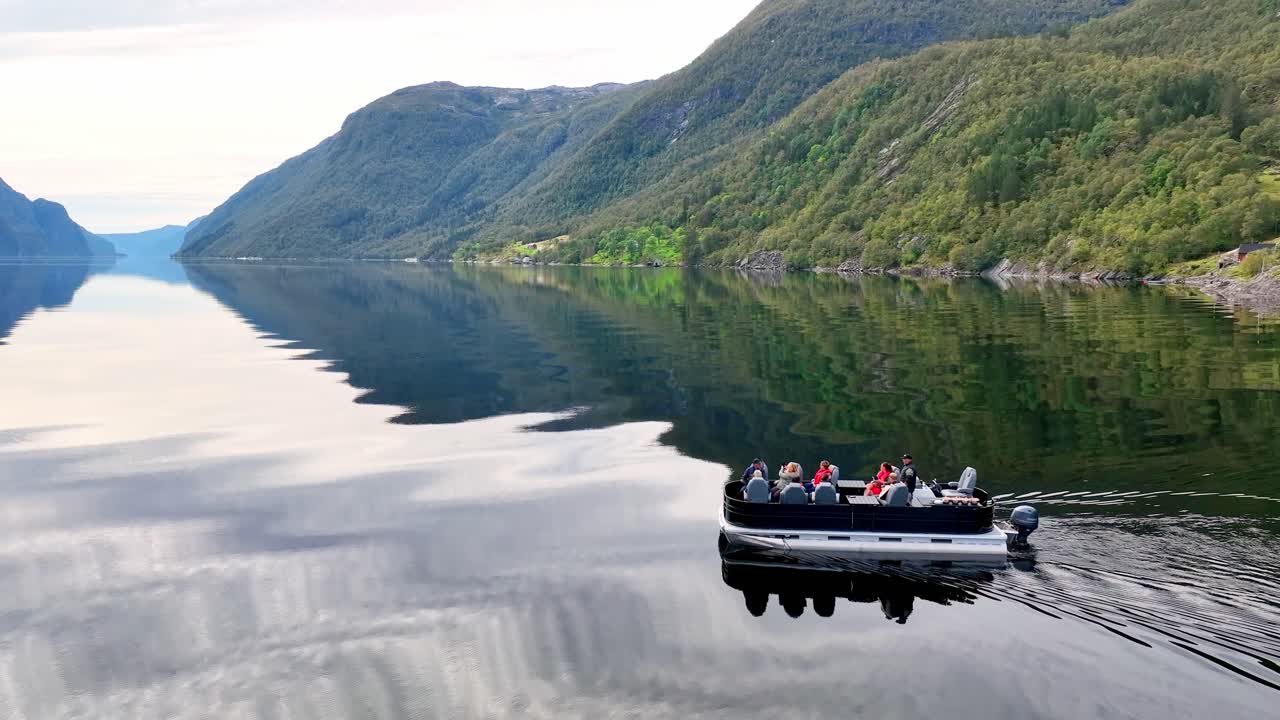 Drone closely follows a pontoon boat in Veafjord as the guide gestures and explains to a happy group of tourists