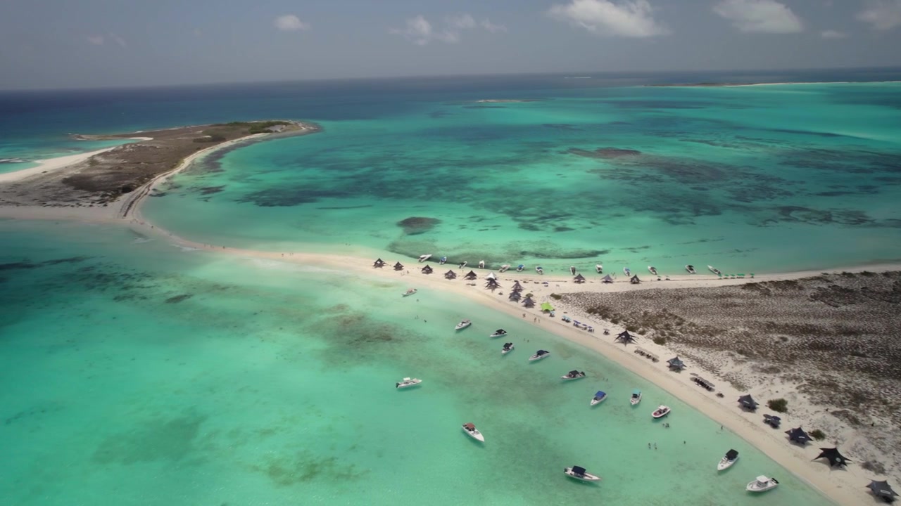 Ripresa aerea con drone dall'alto che spazia su acque turchesi incontaminate e un banco di sabbia tropicale sotto una luce solare brillante