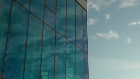 cloud reflections on a blue glass building against a clear sky