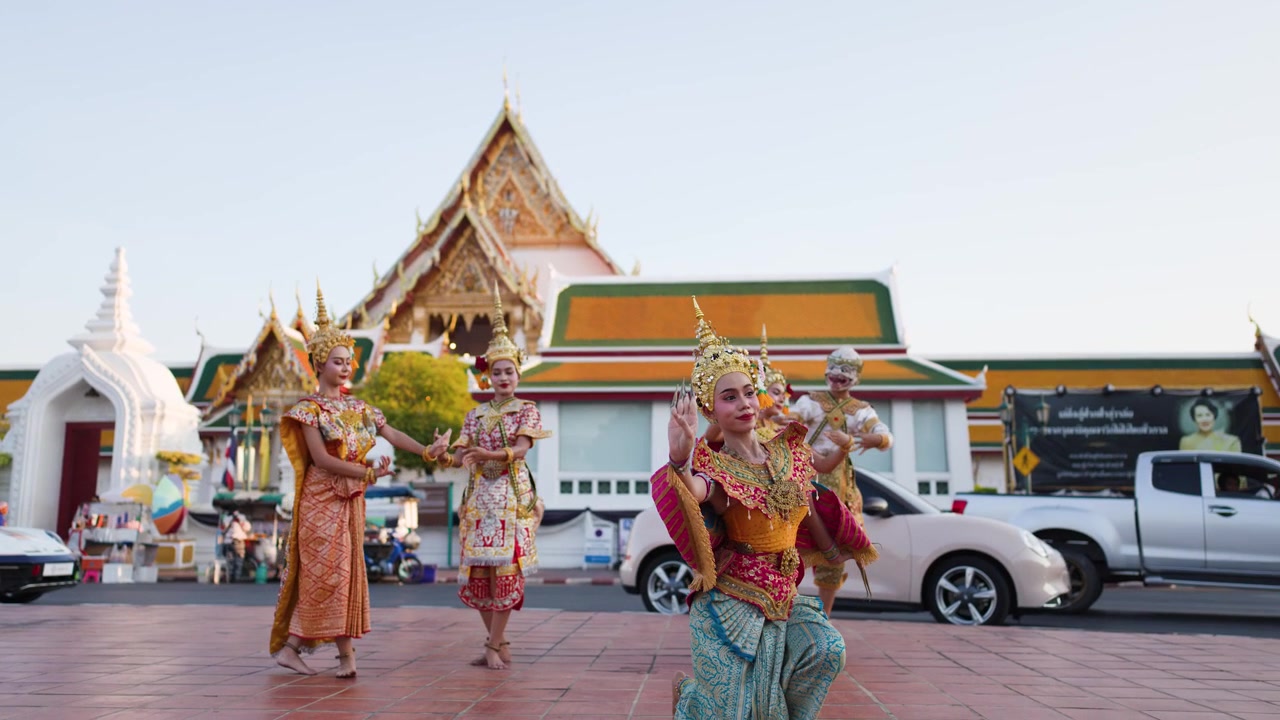 Artisti in sontuosi costumi dorati danzano all'aperto presso un tempio thailandese storico durante il giorno