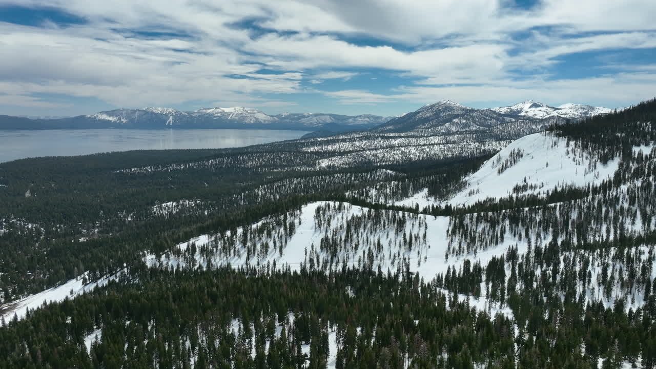 Aerial view rotating over snowy mountains of Tahoe, cloudy, winter day in USA